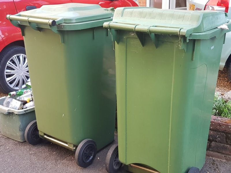 Two green recycling bins and a container for glass recycling