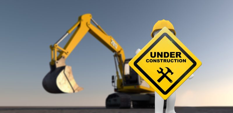 A figure holds up an Under Construction sign. There is a construction digger in the background